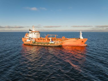 Baltık Denizi 'ndeki bir sığınak mavnasından yakıt ikmali yapılan turuncu petrol tanker gemisinin yüksek açılı drone görüntüsü..