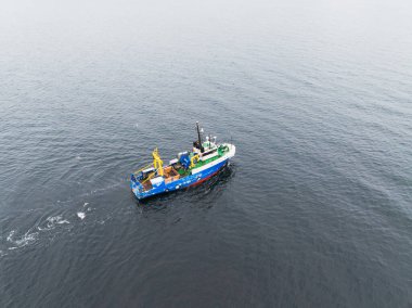 Gündüz vakti Baltık Denizi 'nin sakin karanlık sularında avlanan mavi bir balıkçı teknesinin insansız hava aracı görüntüsü..