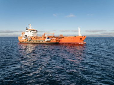 Baltık Denizi 'nin mavi sularında sığınak operasyonu yapan parlak turuncu endüstriyel tanker gemisinin insansız hava aracı görüntüsü..
