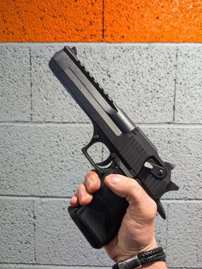 12 Şubat 2026 Tallinn Estonya. Siyah Çöl Kartalı 44 Magnum tabancasını kapalı alandaki bir atış poligonunda gri ve turuncu bir beton bloğa karşı tutan bir elin yakın çekimi..