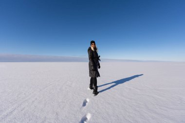 Güneşli bir kış gününde Estonya 'nın Narva-Joesuu plajındaki engin donmuş Baltık Denizi buzunda yürüyen gülümseyen kadın..