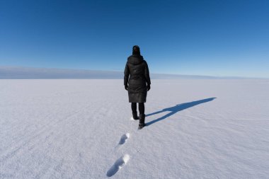 Estonya 'da açık mavi bir gökyüzünün altında donmuş bir kar tarlasında yürüyen bir kadının arka görüntüsü..