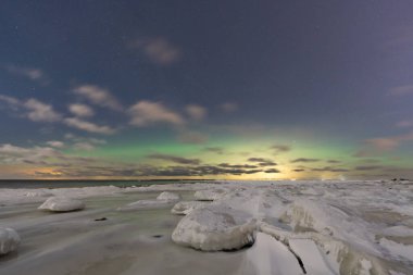 Buz tutmuş Baltık Denizi kıyıları yeşil Kuzey Işıkları Aurora Borealis gece gökyüzünde görünmeye başlıyor..