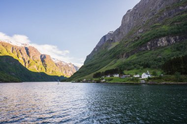 Geleneksel beyaz kilise ve küçük bir köyde evler. Görkemli Norveç fiyortunun derin mavi suları boyunca yuva yapmış..