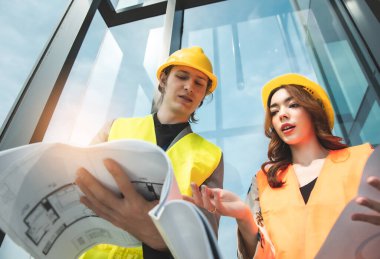 Mekanik fabrika okuma talimatları mühendisleri gülümseyen imalatçı kadın ve erkek, beyaz gökyüzü ve bina kulesinin arka planına güvenerek ayakta duruyorlar. Sanatsal geçmişi parlak insanları yetiştirme sanayisi.