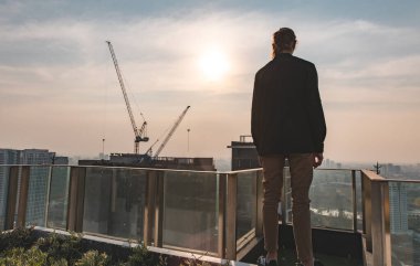 Şehrin yukarısındaki gün batımına bakan bavullu iş adamının arkası. Düşünceli bir zihinle şehir manzarasını dört gözle bekleyen bir yaşam tarzı düşün.