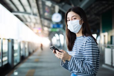 Genç Asyalı kadın ağzını kapatıyor, virüsleri korumak için tıbbi maske takıyor. Diğer insanlardan 1 metre uzakta duruyor COVID-19 virüslerinden uzak duruyor. Sosyal mesafe:.