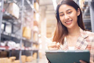 Gülümseyen Asyalı yönetici kadın portresi ayakta duruyor ve depodaki eşyaları kontrol etmek için tablet bilgisayardan ayrıntıları sipariş ediyor..