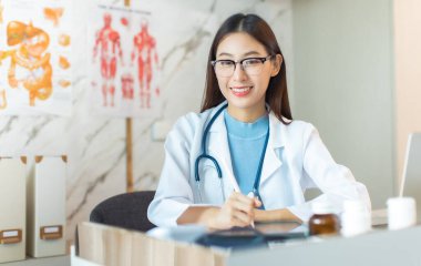 Hastanedeki beyaz önlüklü genç Asyalı kadın doktor portresi. Teletıp, internetteki tıbbi ve sağlık konsepti. Doktor iş için dizüstü bilgisayar kullanıyor. Uzaktan hasta danışma desteği için uzaktan tıbbi yardım.