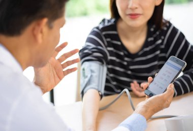 Kıdemli doktor steteskopla sfinometre kullanıyor. Hastanedeki bir hastanın tansiyonunu ölçüyor..