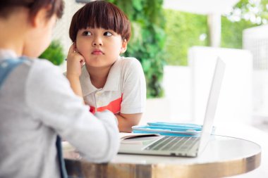 Asyalı erkek ve kız bilgisayar başında masa başında çalışıyor, akıllı çocuklar el yazısını deftere yazıp karantina ve evde eğitim kavramlarını kullanarak öğreniyorlar..