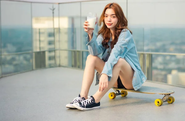 アジアの若い女性は美しい夏の日に屋外でスケートボードやスケートボードをサーフィン ハッピー若いです女性幸せな遊びサーフスケートで屋上都市 Bangkok ロイヤリティフリーのストック画像