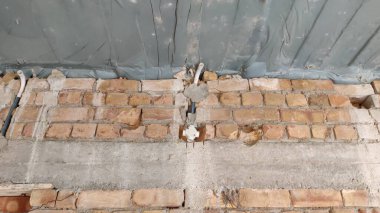 Close up shot of a brick wall with damaged plaster and exposed pipes under a plastic covered ceiling