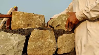 29 Ekim 2025 'te Pakistan' da günlük işçi hayatını gösteren parlak güneşin altında taş duvarı betonla onaran çok çalışkan bir Pakistan ustası.