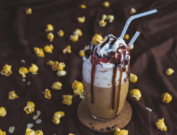 Glass of coffee with sour cream, caramel popcorn and chocolate
