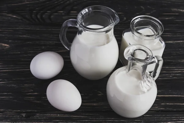 Молочные банки и яйца на деревянном фоне — стоковое фото