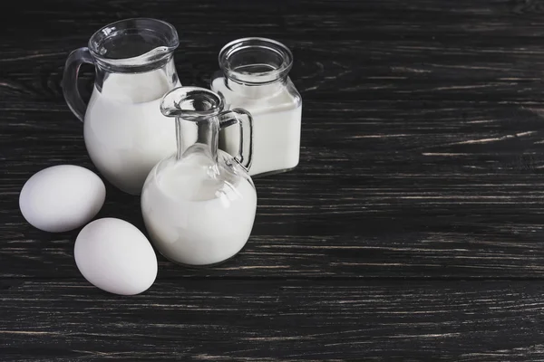 Молочные банки и яйца на деревянном фоне — стоковое фото