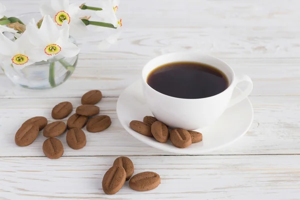 Taza de café, galletas y narcisos sobre fondo de madera blanca — Foto de Stock