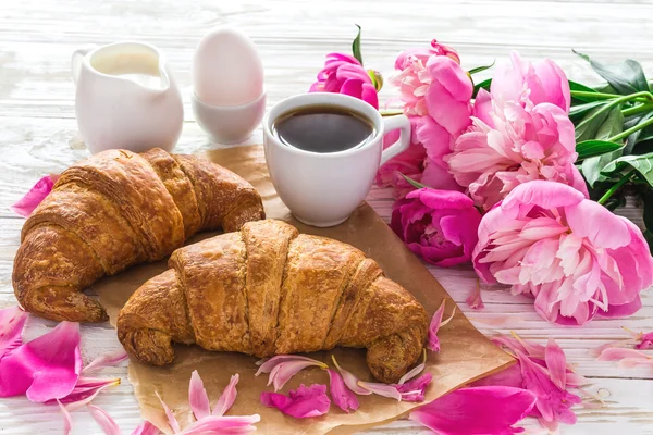 Cup of coffee, croissants, milk jar and peonies flowers — Stock Photo, Image