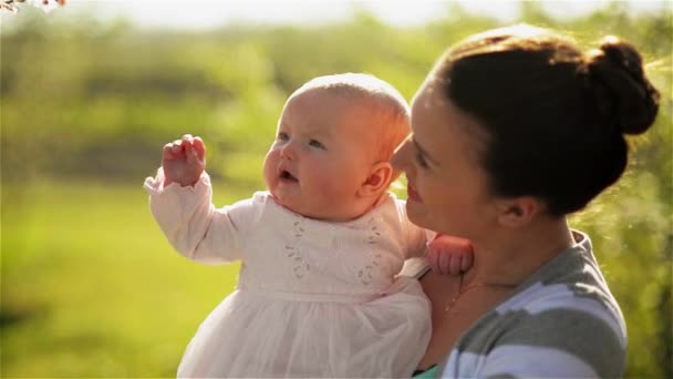 Hermosa joven madre jugando con su bebé recién nacido en un exuberante jardín, riendo — Vídeo de stock