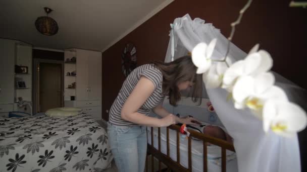 Красива молода мати стоїть біля ліжка своєї новонародженої дитини — стокове відео