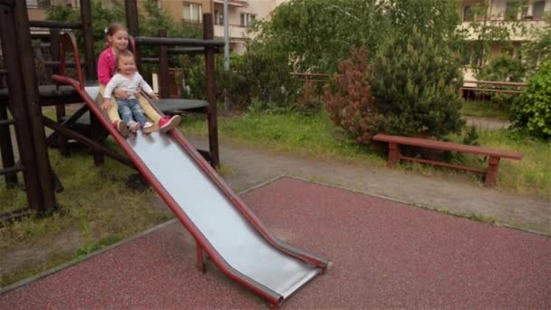 Zwei kleine süße Mädchen haben großen Spaß beim Rutschen auf dem Spielplatz — Stockvideo