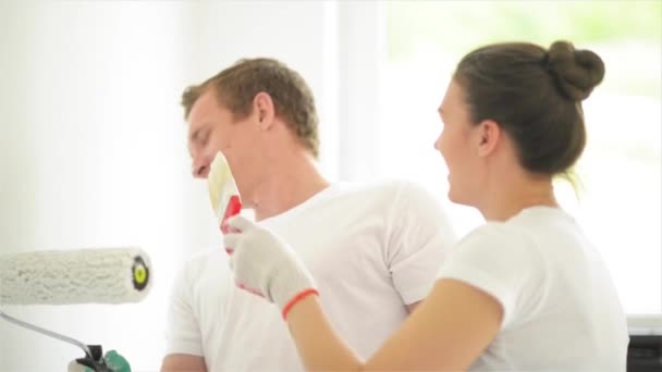 Hermosa pareja pintar las paredes en un nuevo apartamento, riendo y divirtiéndose — Vídeo de stock