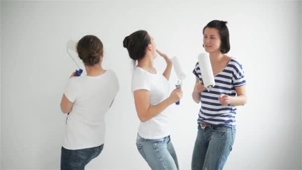 Los amigos hacen reparaciones en casa. Chicas divertidas bailan y pintan las paredes en el piso — Vídeo de stock