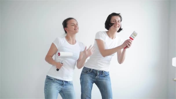 Dos chicas cantando en el rodillo de pintura, amigos están haciendo reparaciones y bailando — Vídeos de Stock