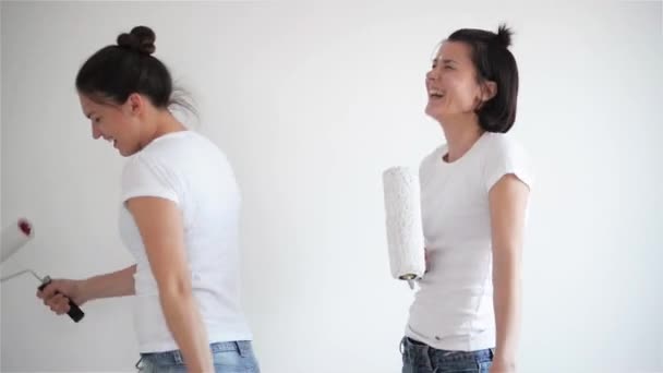 Dos chicas cantando en el rodillo de pintura, amigos están haciendo reparaciones y bailando — Vídeo de stock