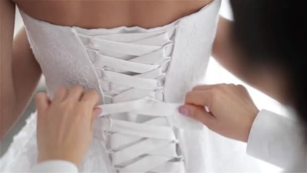 Подружка невесты шнурует белое свадебное платье для красивой невесты, готовит свадьбу — стоковое видео