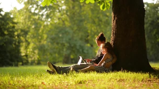 Dos chicas usando la tableta en un hermoso parque, un cálido día de verano — Vídeos de Stock