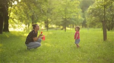 Anne ve kız açık sabun köpüğü üfleme. Anne-baba ve çocuk parkında eğleniyor.