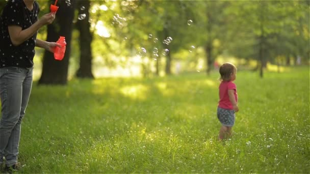 Mamman och flickan blåser såpbubblor utomhus. Förälder och barn har roligt i park. — Stockvideo