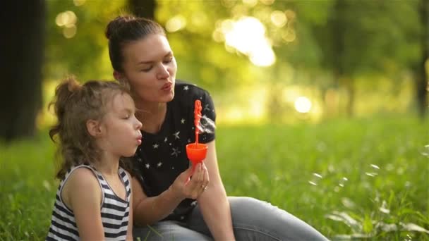 Hermosa madre con su hija en la naturaleza haciendo burbujas de jabón y riendo — Vídeo de stock