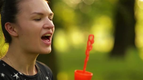 Schöne junge brünette Mädchen weht Seifenblasen im Freien. — Stockvideo