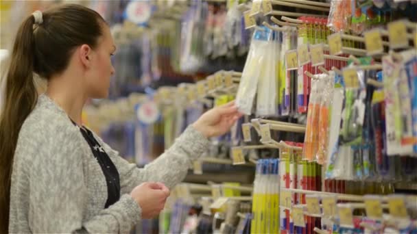 Jovem mulher bonita comprando artigos de papelaria para a escola, bela mãe escolher canetas e ferramentas em um supermercado para seus filhos — Vídeo de Stock
