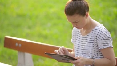 Sevimli genç kadın parkta, güzel kadın parkta bir bankta oturmuş ve tablet kullanma Bahçe, genç kız öğrenci bir bankta bir tablet kullanarak tablet ile
