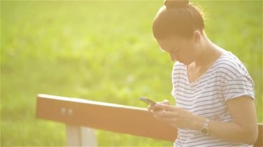 Parkta bankta oturmuş smartphone kullanan genç gülümseyen kadın. Güzel Avrupa kız manifatura telefon