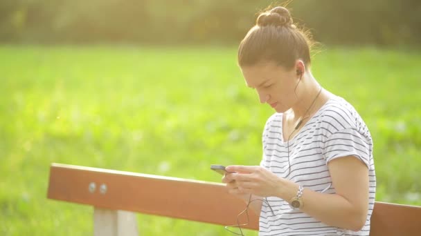 Woman listening to the music from a smart phone with headphones in a park, beautiful woman using smartphone with headphones — Stock Video