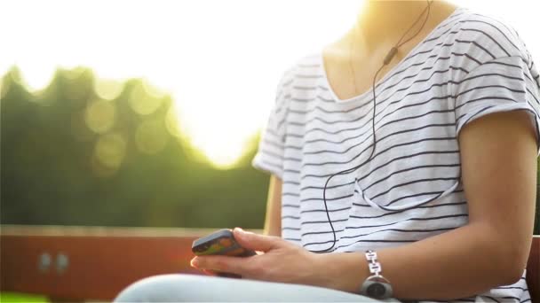 Femme écoutant la musique d'un téléphone intelligent avec écouteurs dans un parc, belle femme utilisant un smartphone avec écouteurs — Video