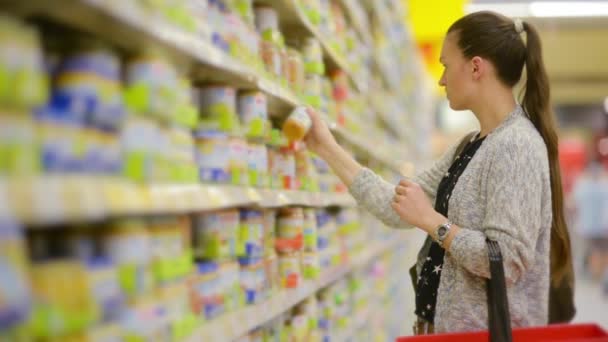 Jonge vrouw kiest babyvoeding in de supermarkt, moeder kiest voedsel voor hun kind in de markt, meisje staat in de buurt van het schap van de supermarkt en selecteert de producten — Stockvideo