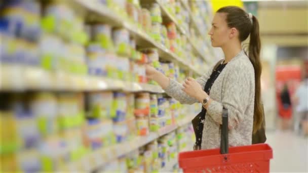 Junge Frau wählt Babynahrung im Supermarkt, Mutter wählt Lebensmittel für ihr Kind auf dem Markt, Mädchen steht neben dem Supermarktregal und wählt die Produkte aus — Stockvideo