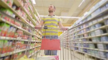 Tam süpermarket adamla trolley yaklaşan kamera ve mutlu bir şekilde gülümseyerek, genç adam süpermarket ürünleri seçer, adam deposundaki içecekler satın