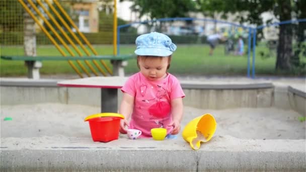 Bambina seduta nella sabbiera e che gioca con gli stampi nel parco giochi, i bambini che fanno forme all'aperto — Video Stock