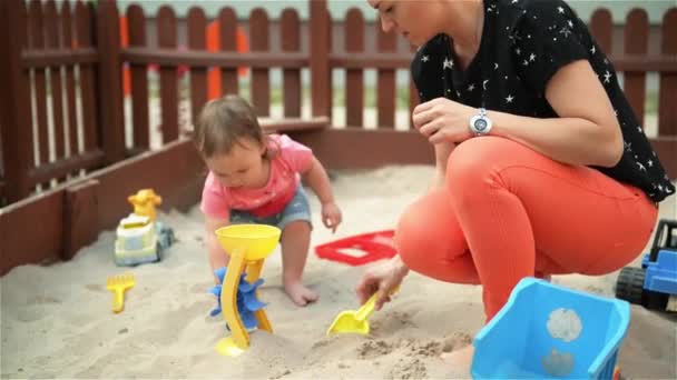 Moeder en baby dochter spelen in de zandbak en het maken van vormen, mooie jonge moeder besteedt tijd met haar kinderen buiten — Stockvideo