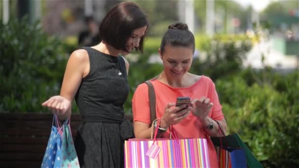 Détendez-vous après une expérience d'achat réussie, Jeune fille avec des sacs à provisions colorés voir quelque chose sur votre smartphone . — Video