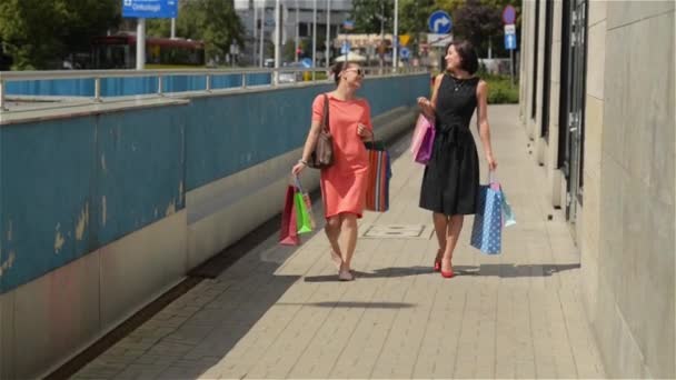 Amigos felizes com sacos de papel de compras andando na cidade, mulheres bonitas deixando o shopping depois de uma compra bem sucedida — Vídeo de Stock