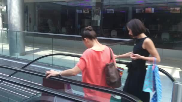 Dos chicas bajando las escaleras en escaleras mecánicas en el centro comercial, amigos están de compras en una tienda, mujeres haciendo compras en la tienda — Vídeos de Stock