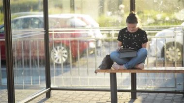 Otobüs durağı, bir istasyonu günbatımı arka plan oturan kadın araçta beklerken kullanım tablet beyaz kadın trendy ile büyüleyici genç bak